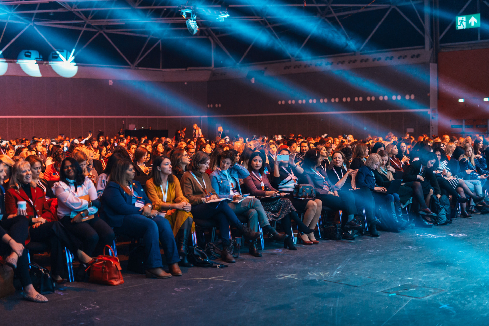 Large keynote audience at a product launch produced by Memories in Motion, lit with dramatic cyan stage beams for the brand reveal moment